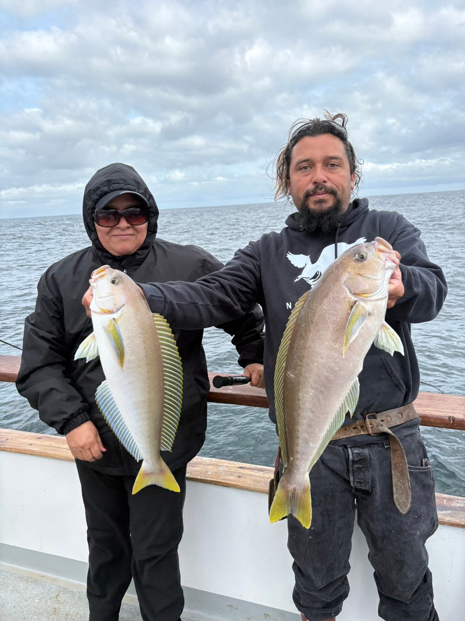 Two anglers holding large fish on boat