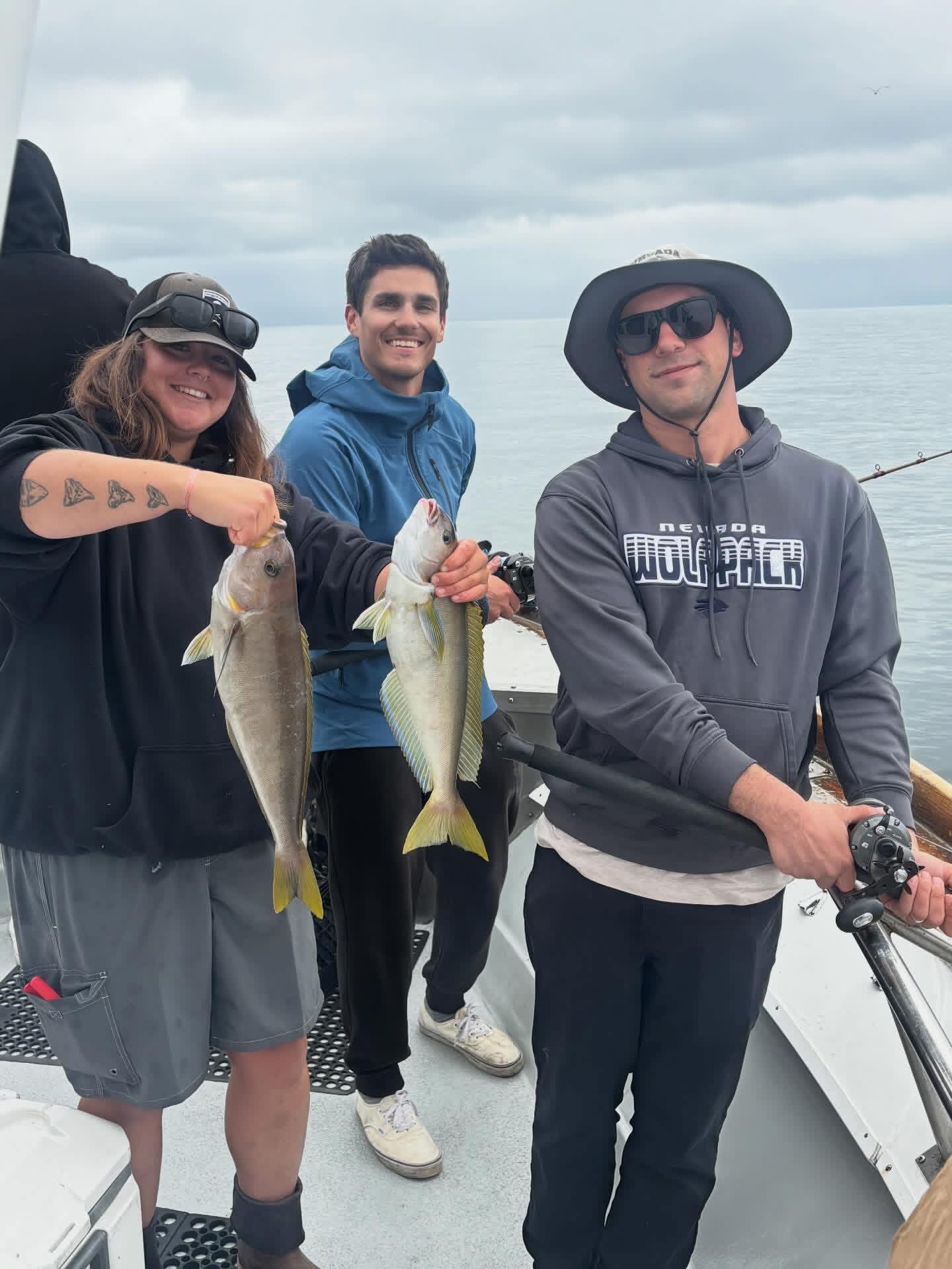 Three anglers on boat holding two fish