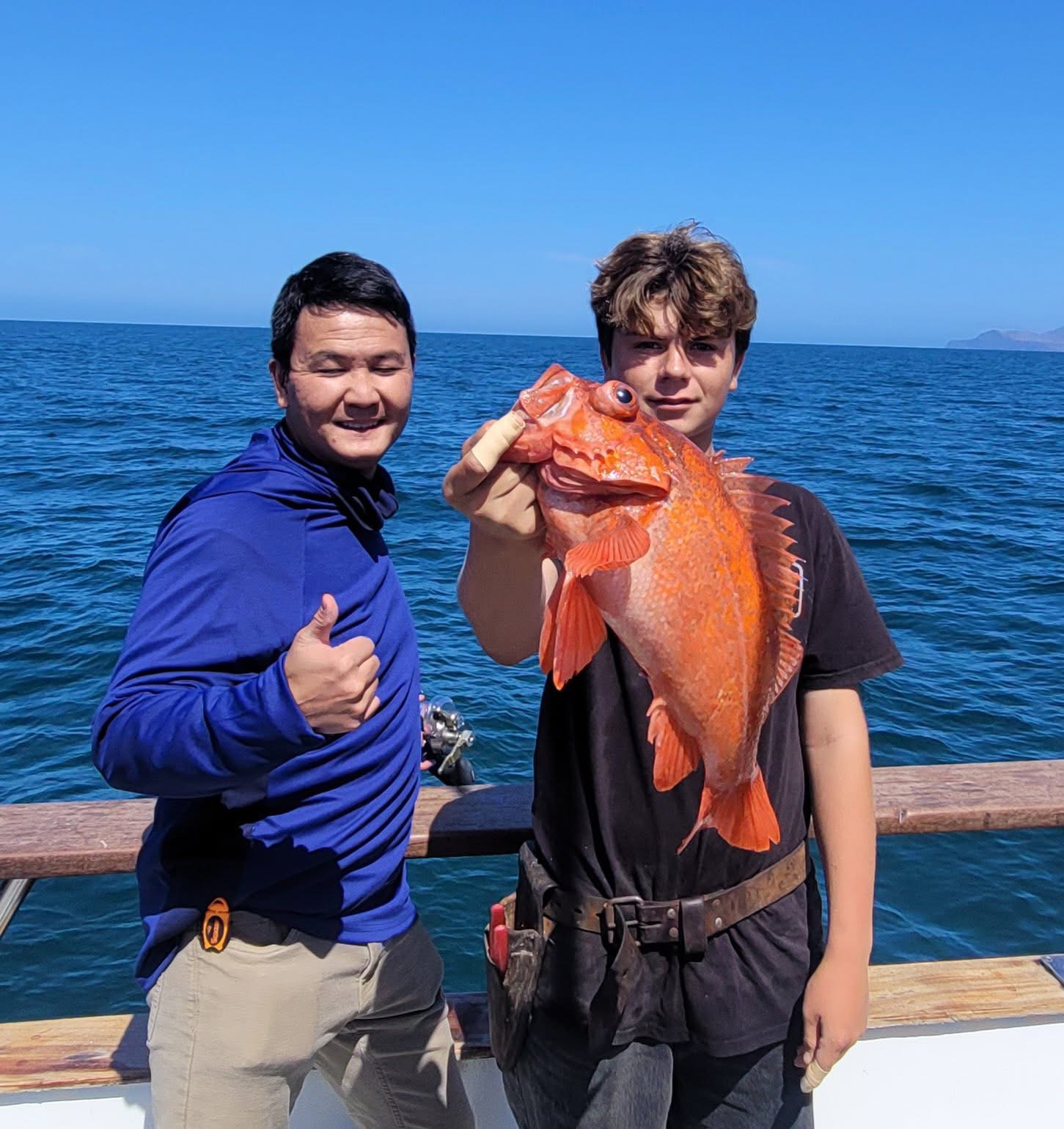 Two people on boat holding large orange fish