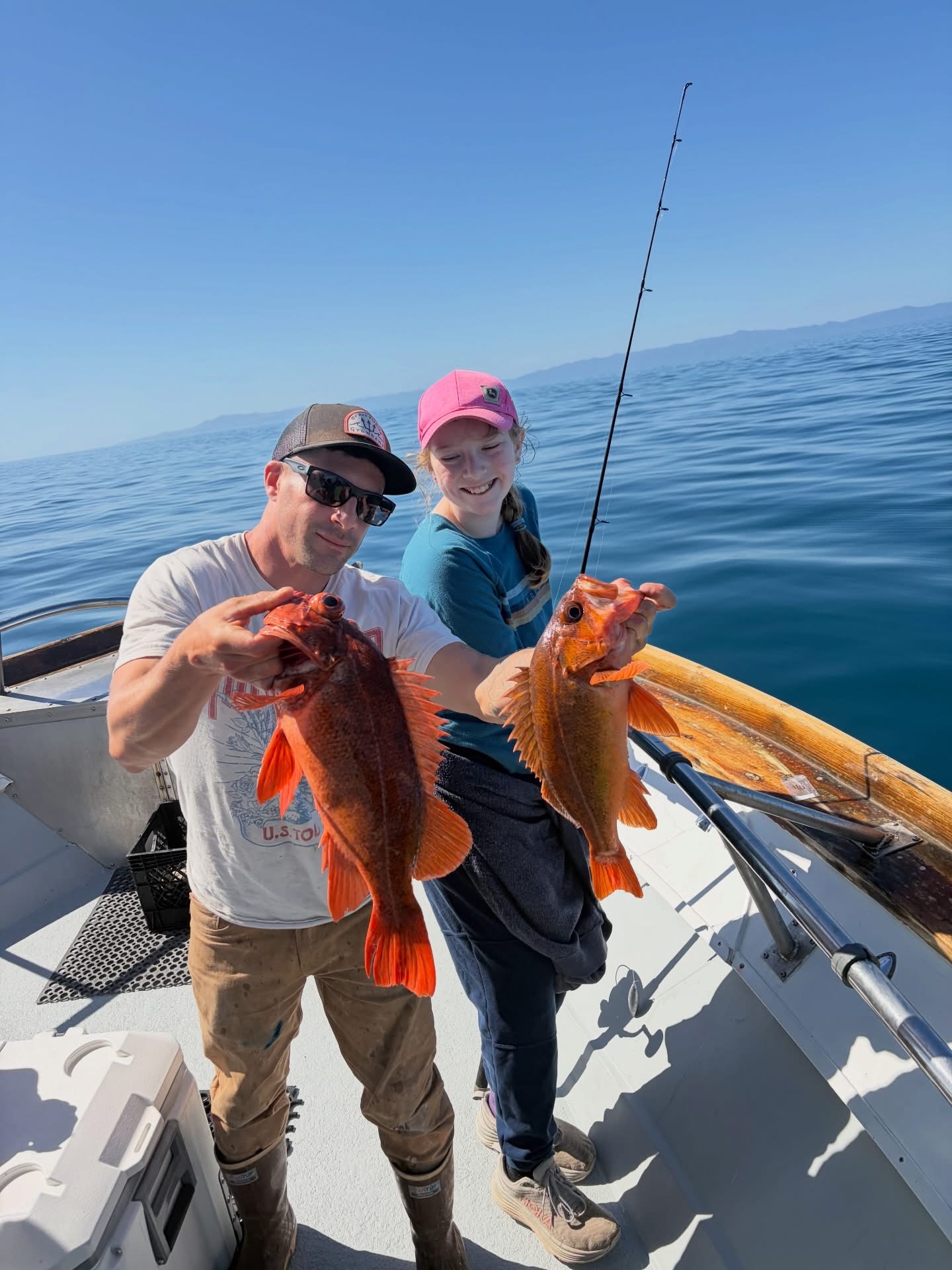 Two anglers on boat holding bright orange fish
