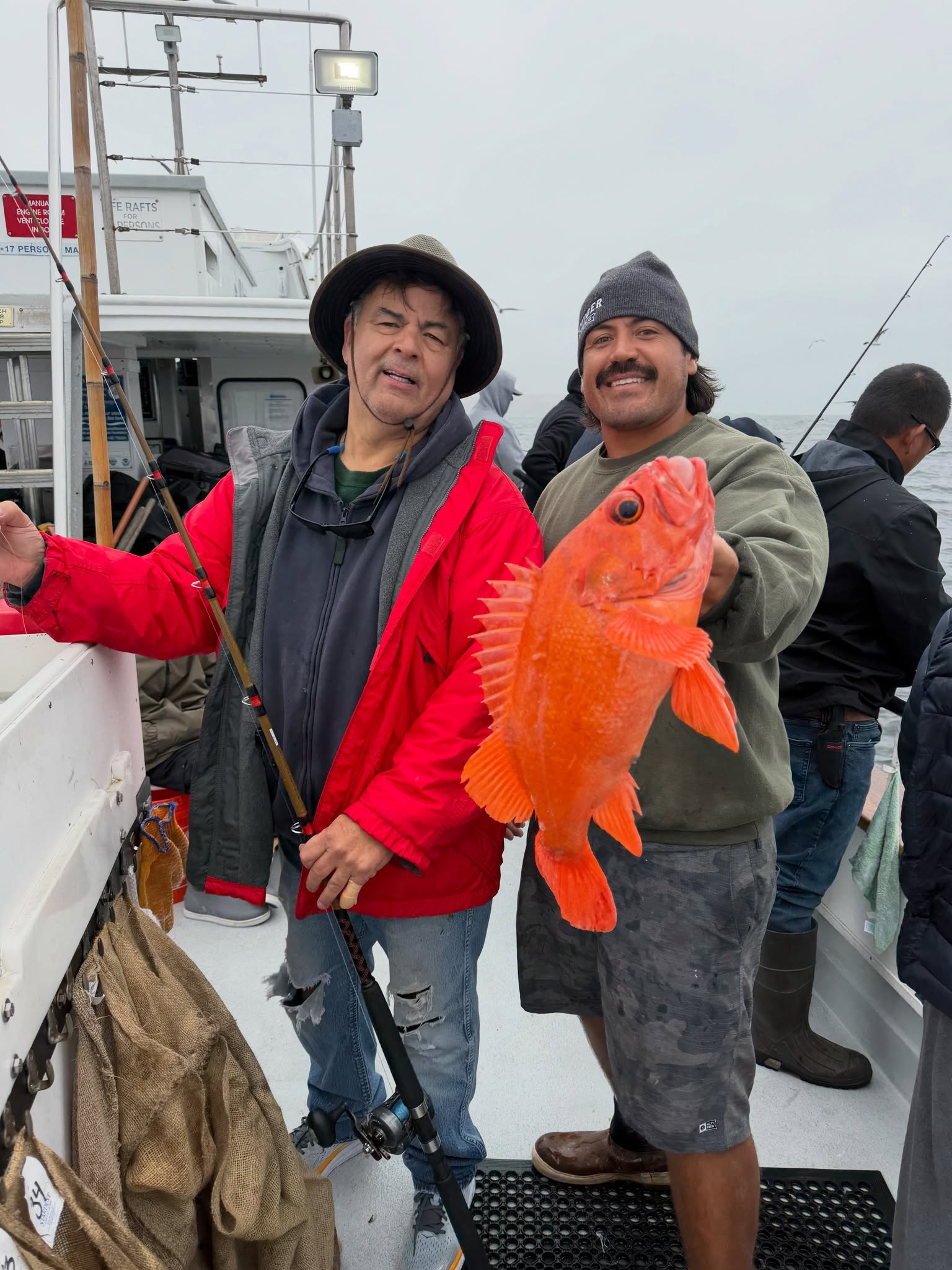 Two fishermen on boat holding large orange fish