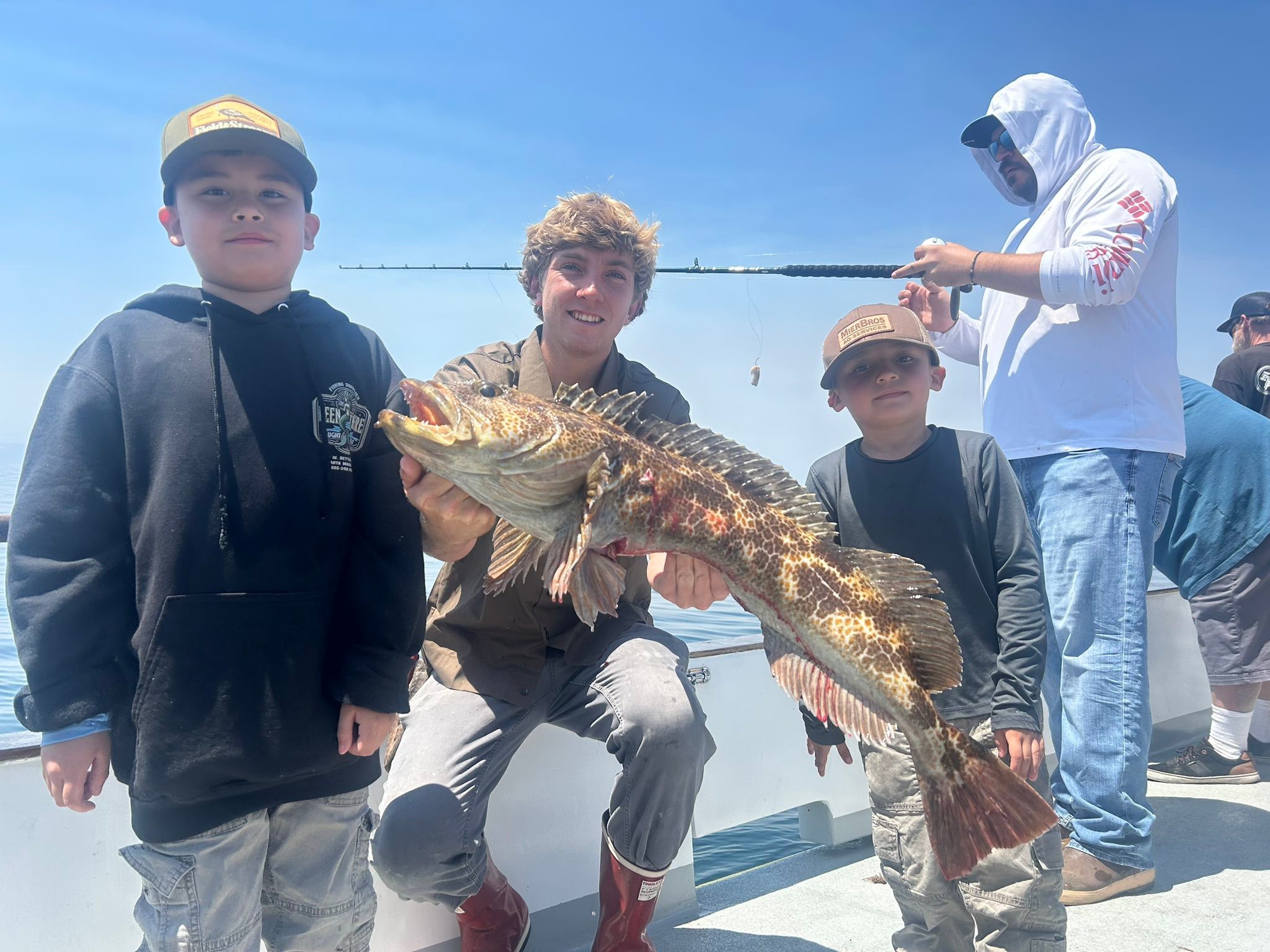 Teen holding large fish on boat with boys