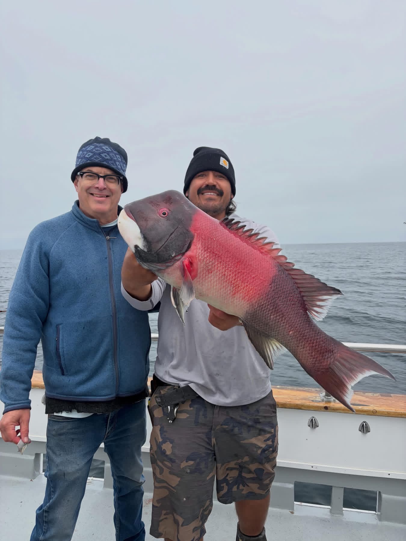 Two men holding large red fish on boat