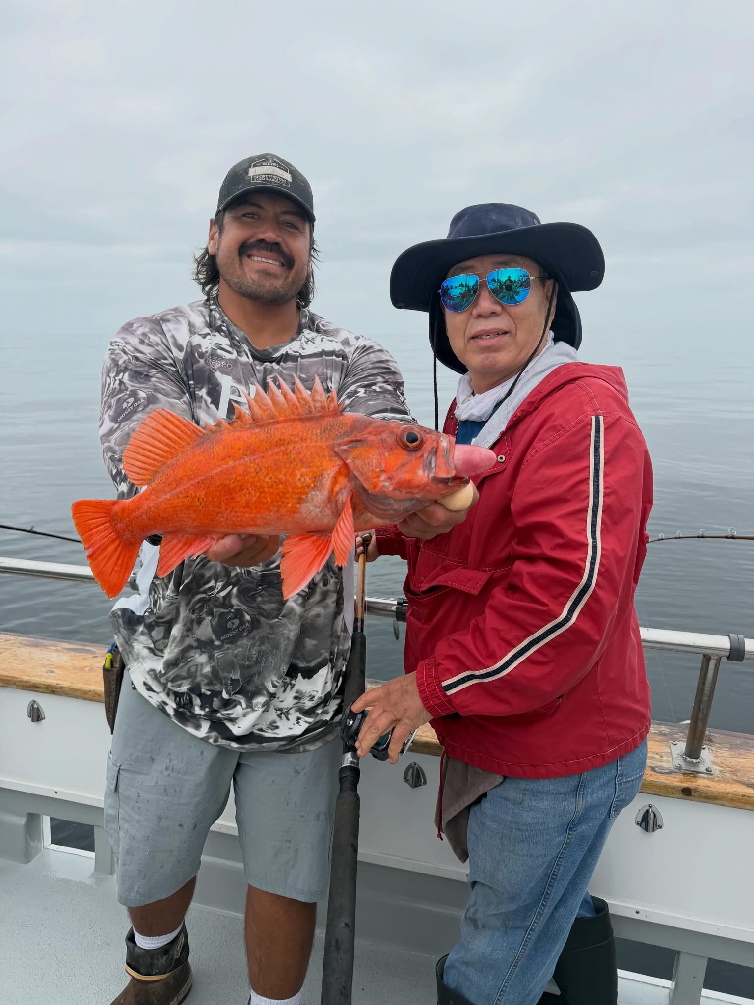 Two anglers on boat holding large orange fish