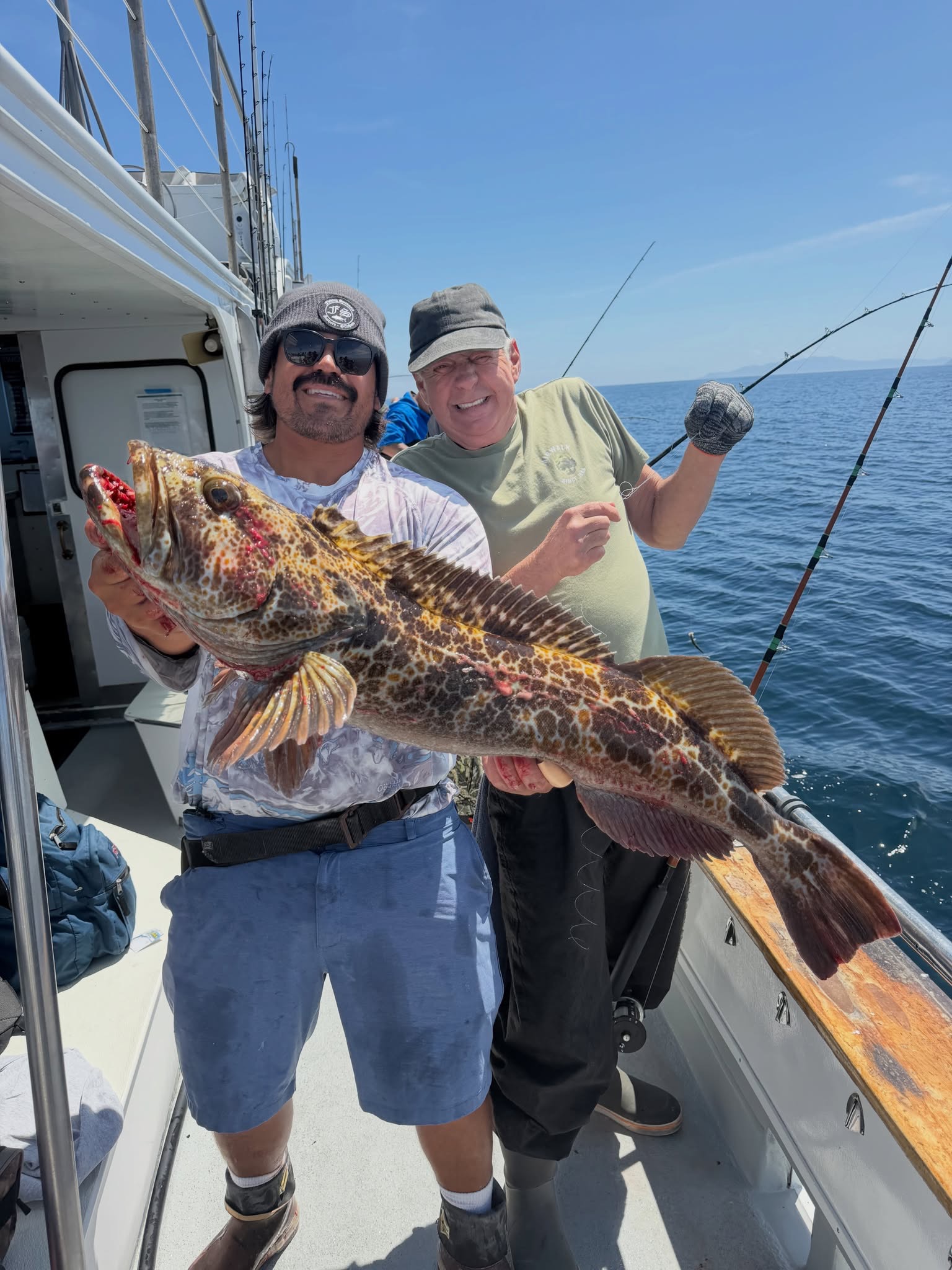 Two fishermen on boat holding large spotted fish