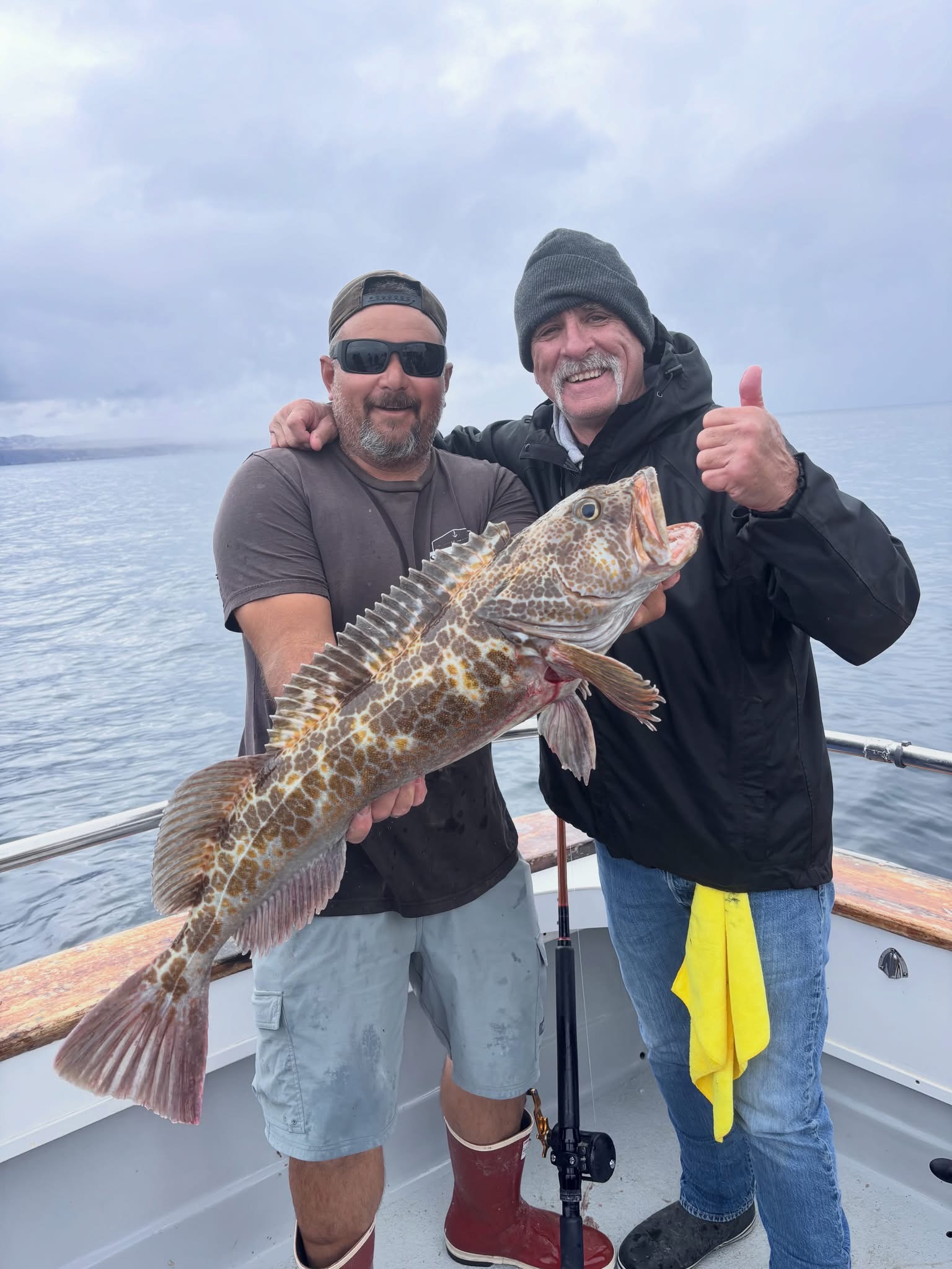 Two men holding large spotted fish on boat