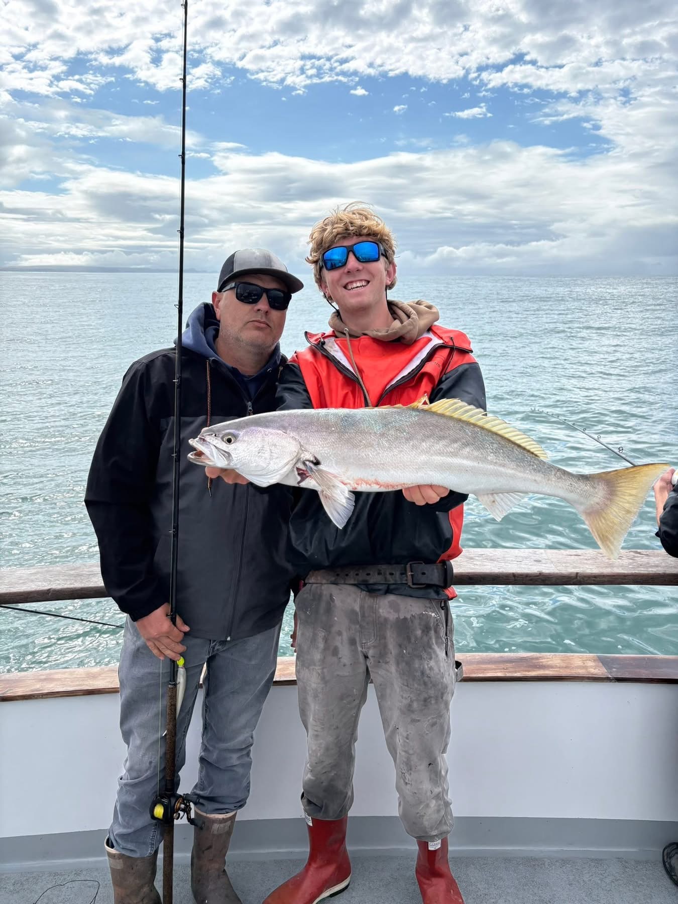 Two fishermen holding large fish on boat