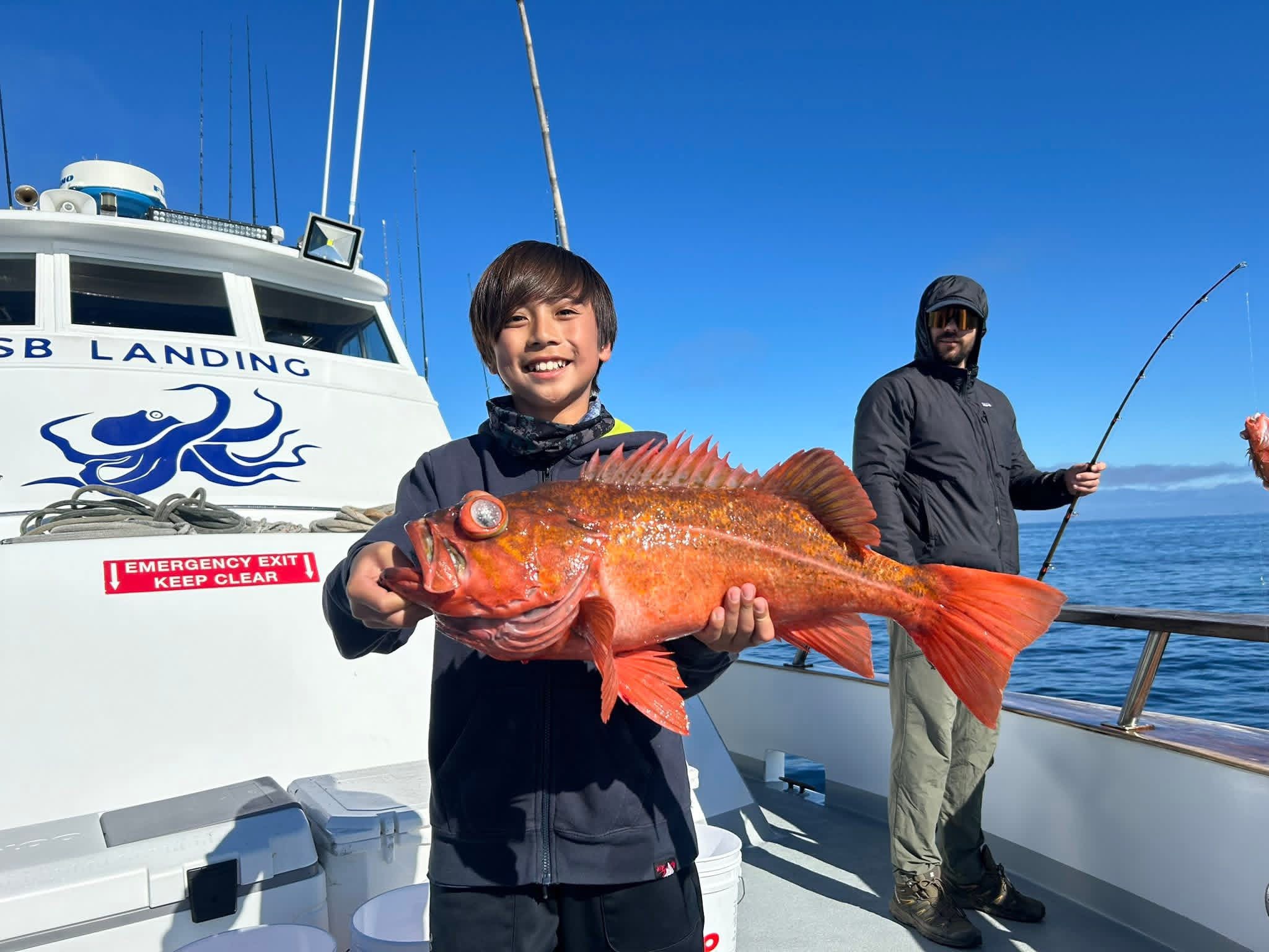 Smiling boy holding large orange fish on boat