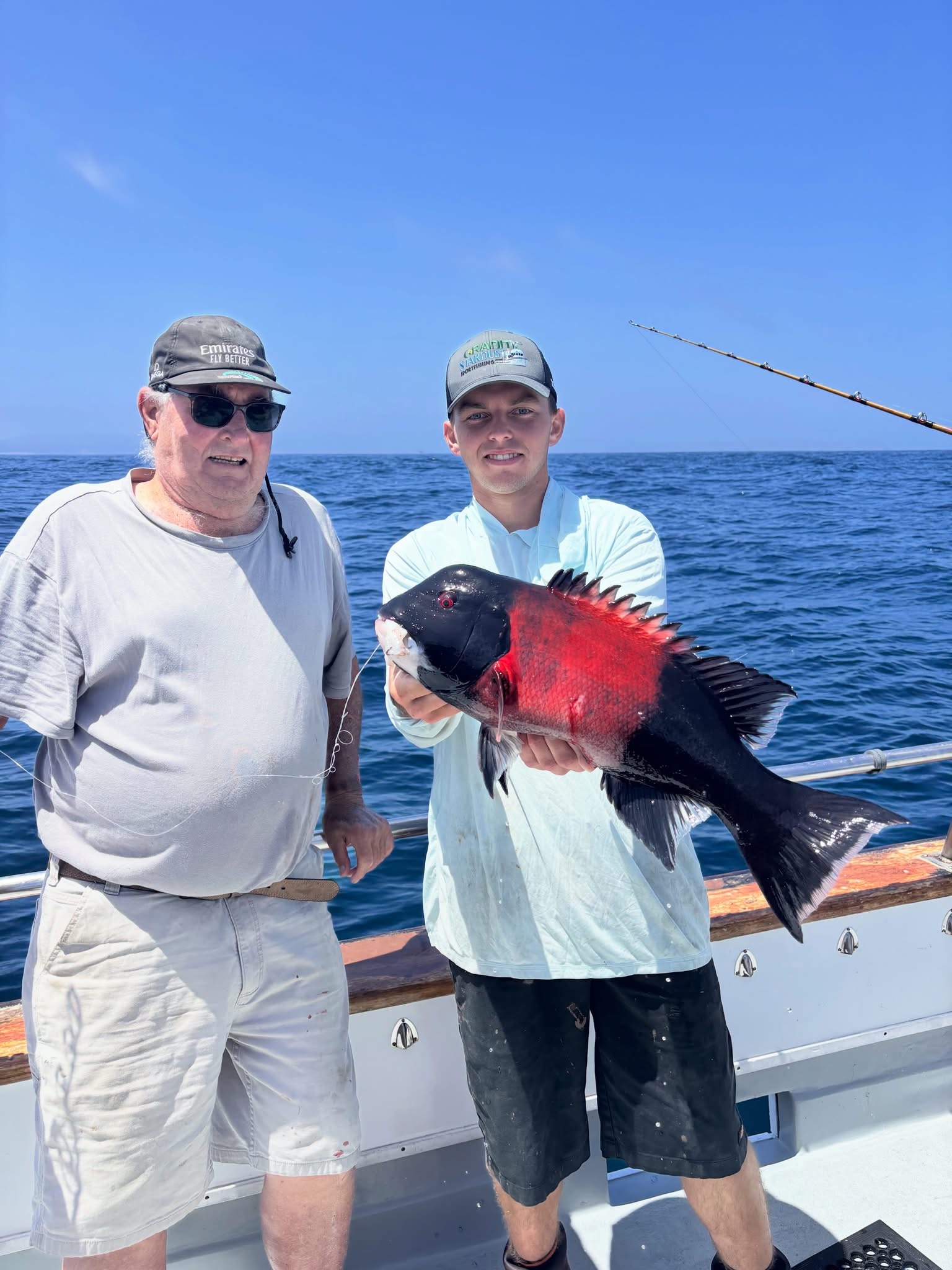Two fishermen on boat holding large red fish