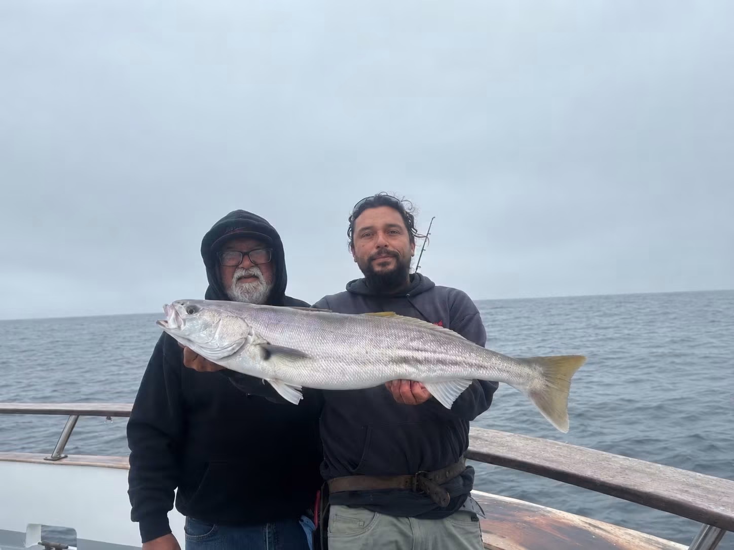 Two fishermen holding large fish on boat