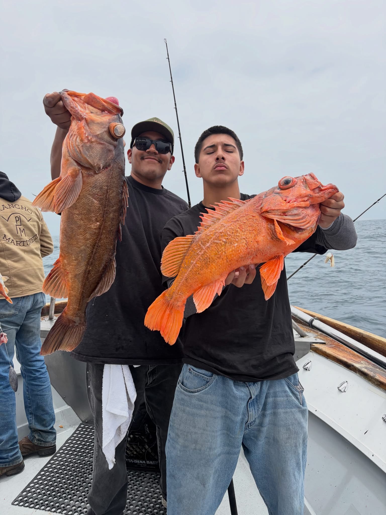Two men on boat holding large orange fish