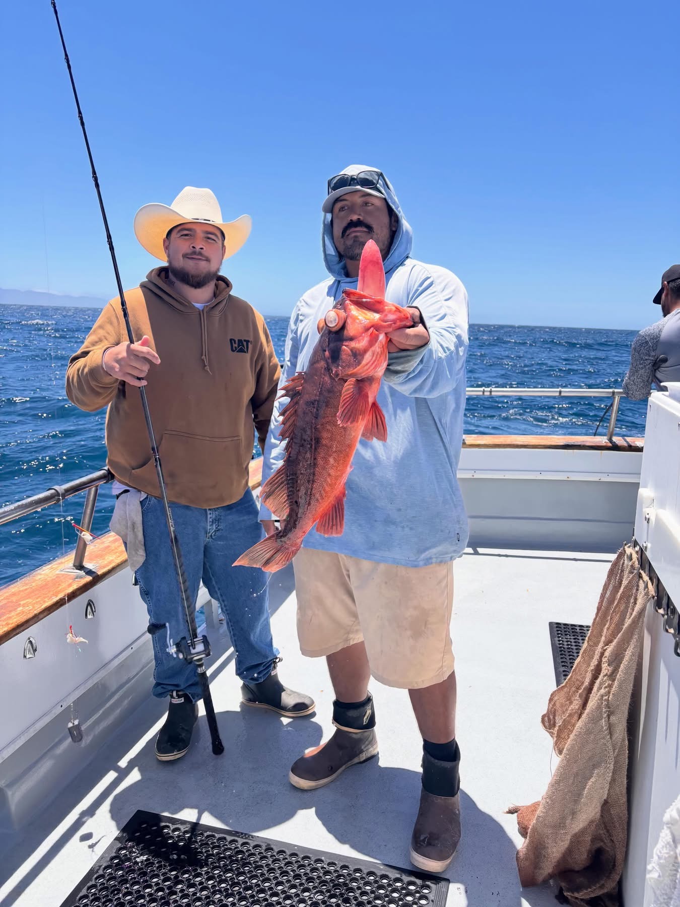 Two fishermen on boat holding large red fish