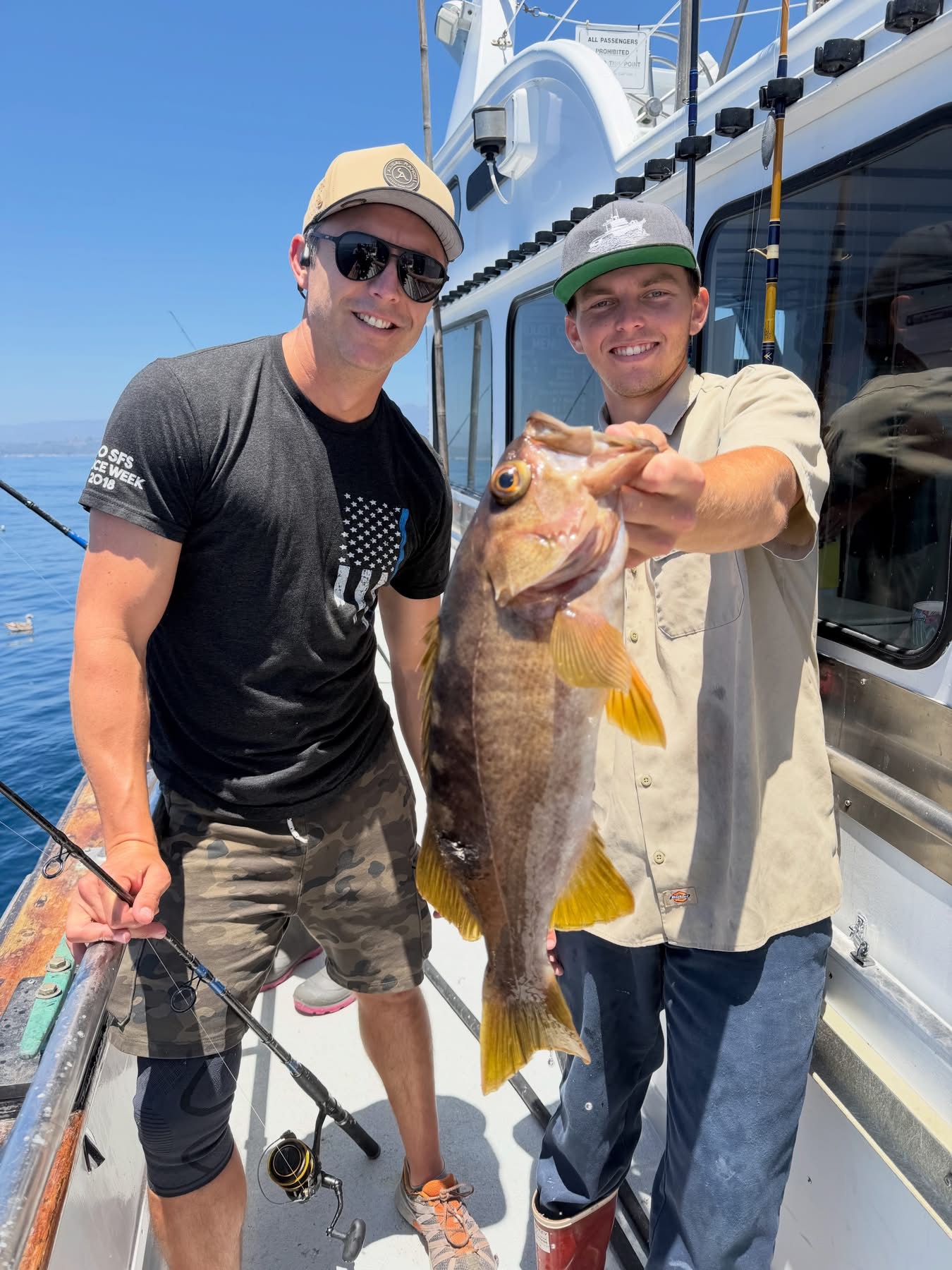 Two fishermen on a boat holding large fish