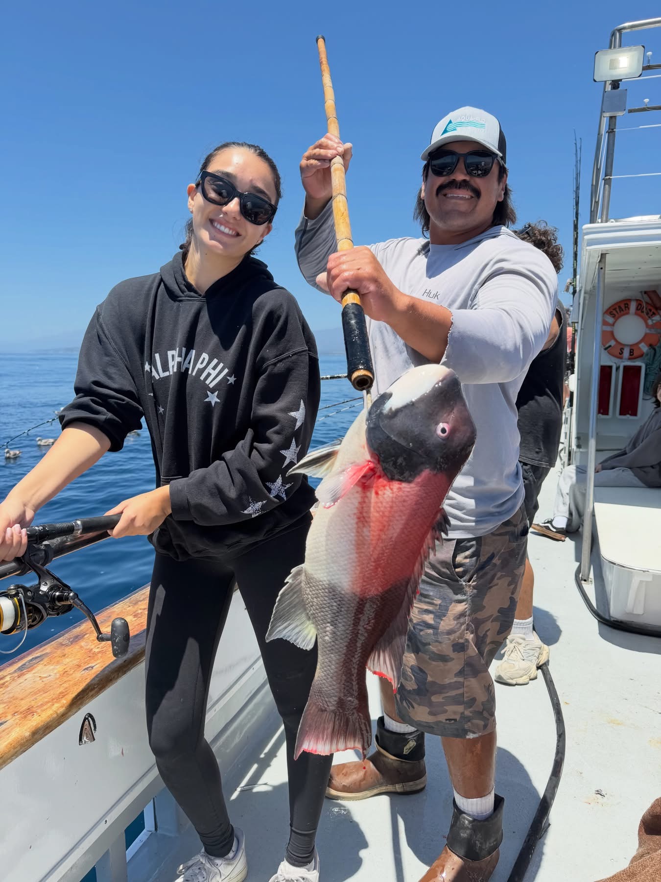 Two people holding large colorful fish on boat