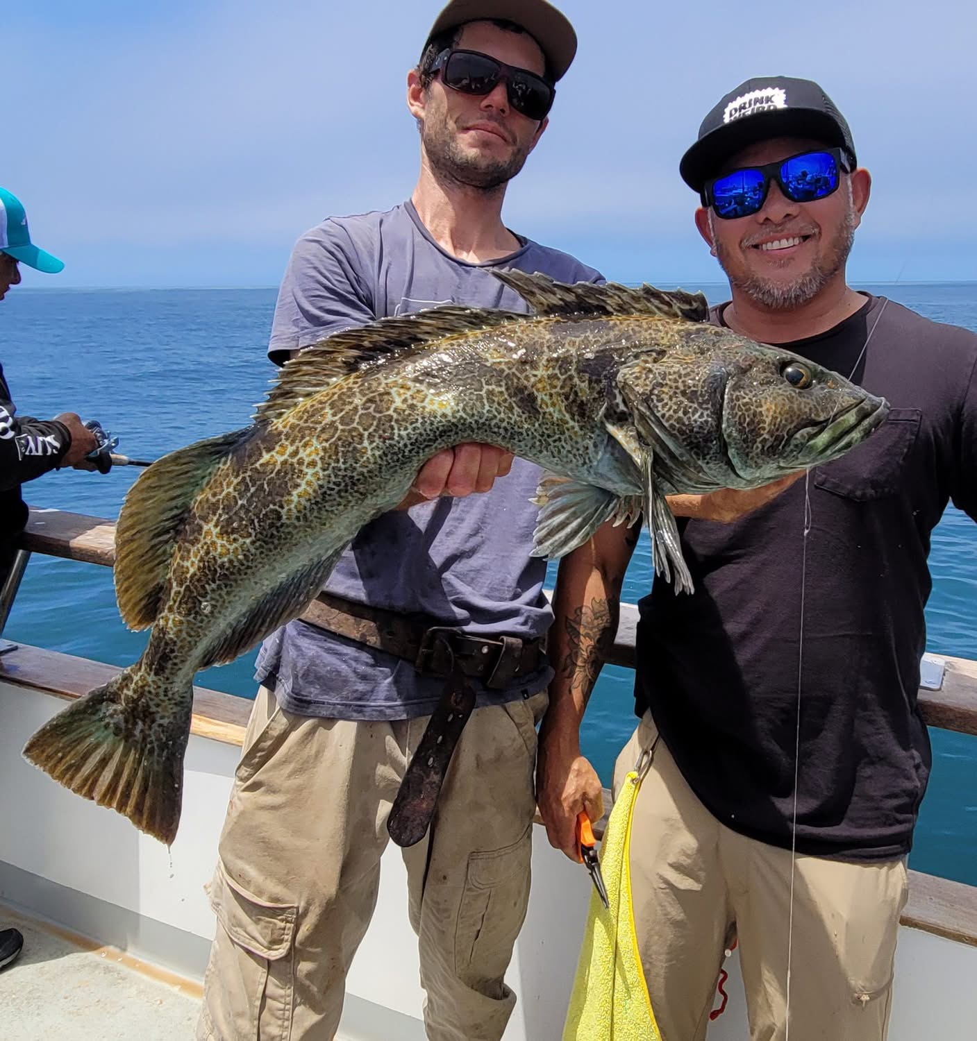 Two anglers holding large lingcod on boat